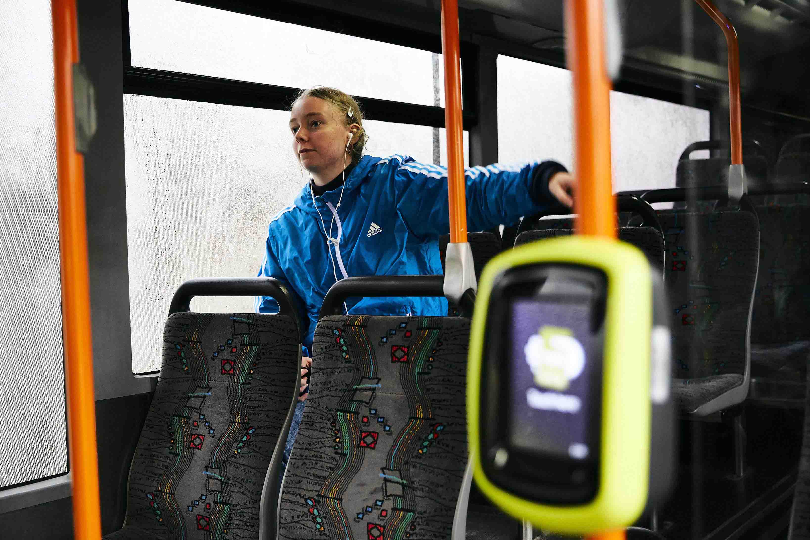 Image shows a young woman travelling on a bus. There is a myki card reader in the foreground.
