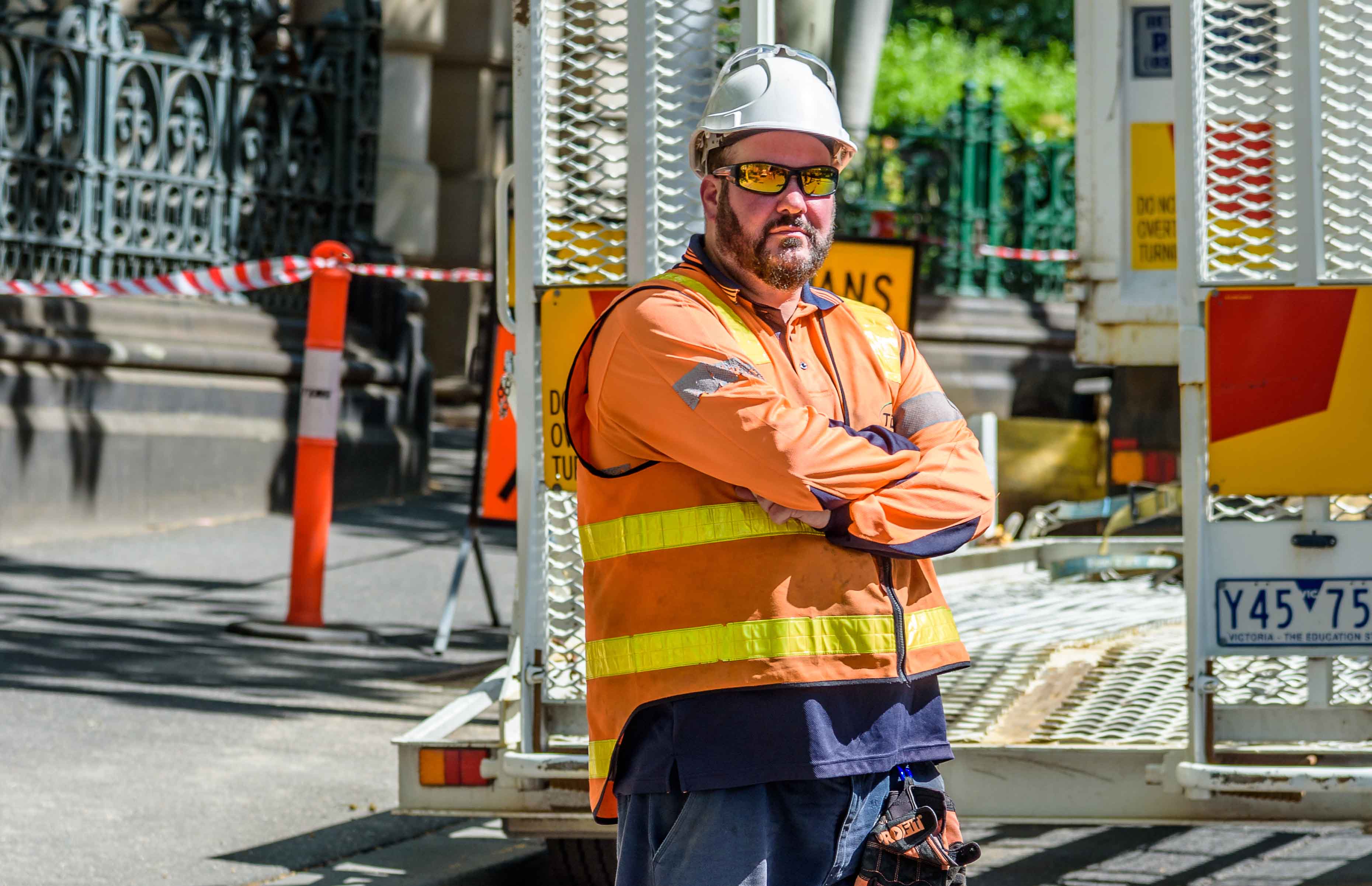 Photo shows a man at a work site. He is wearing high-vis clothing, a hard hat and sunglasses. His arms are crossed in front of him.