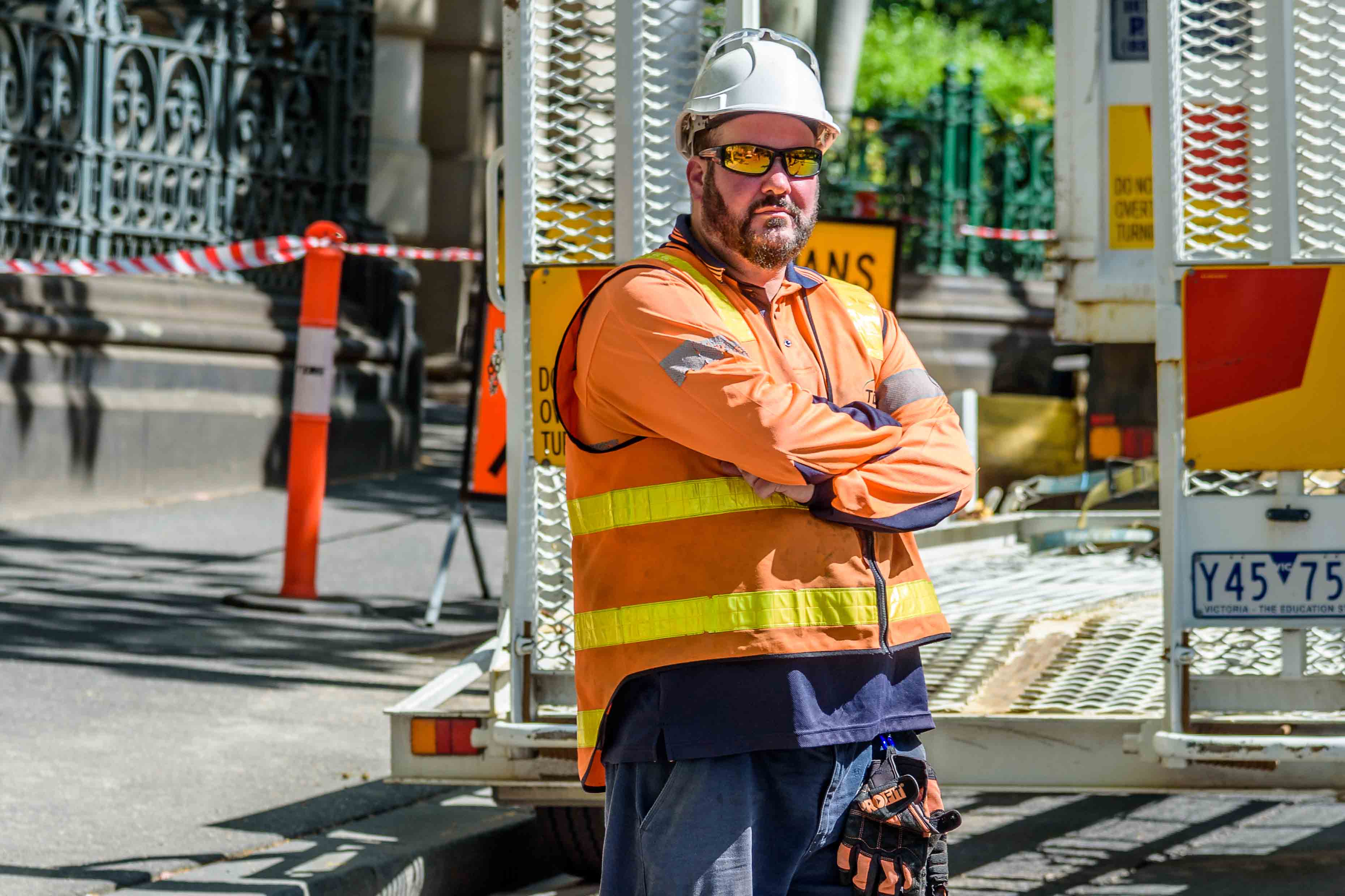 Photo shows a man at a work site. He is wearing high-vis clothing, a hard hat and sunglasses. His arms are crossed in front of him.